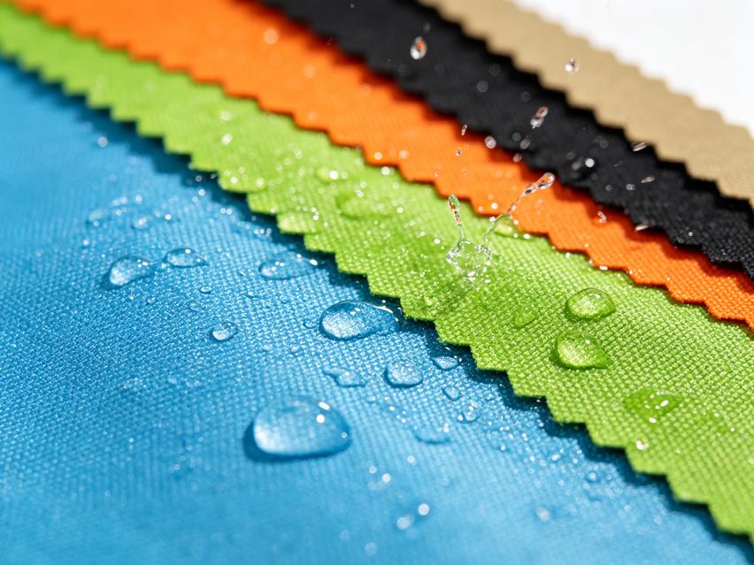 Multicolor oxford fabric sample swatches with water beads demonstrating waterproof coating.